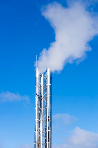 Silver pipes with smoke in the blue sky. vertical frame. Boiler. High quality photo