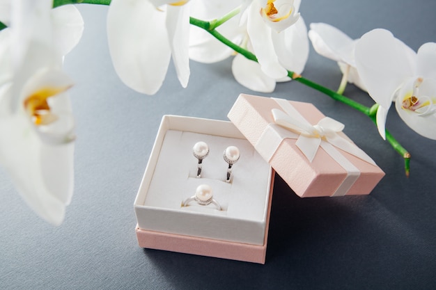 Silver ring and earrings with pearls in gift box with white orchid flower. Present for holiday. Fashion accessories