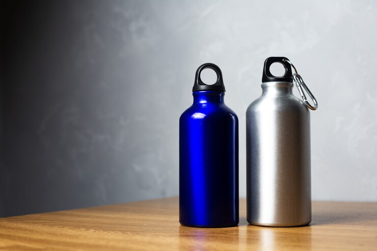 Silver and shiny blue thermo bottle on wooden table.