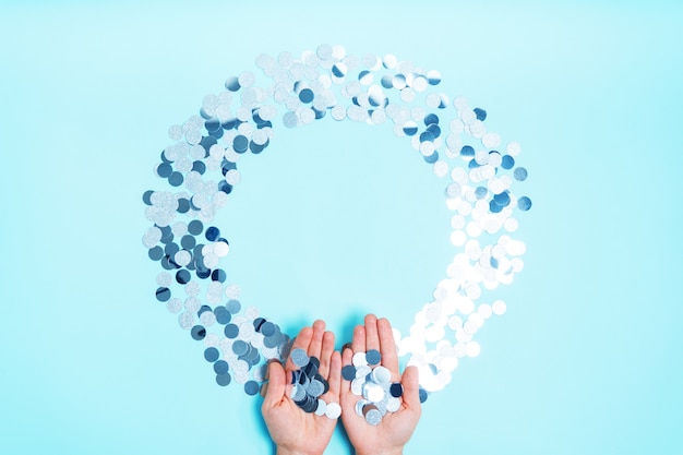 Silver shiny confetti in the form of a round frame on a blue background with a copy of the space.