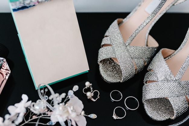 Silver shoes earrings and rings composition isolated on the black background Accessory bridal Wedding rings and sandal Shoe with crystal Engagement Close up