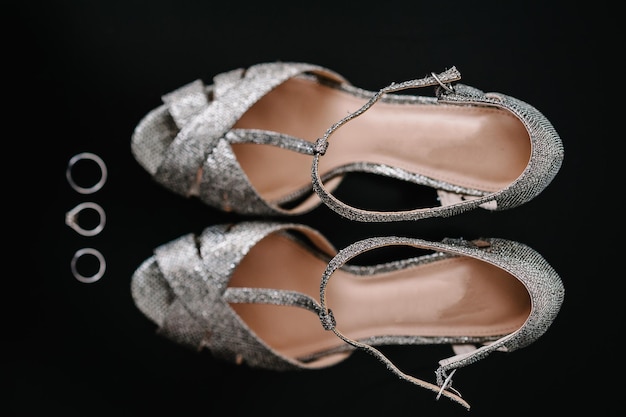 黒の背景に分離されたシルバーの靴とリングの構成アクセサリー花嫁の靴結婚指輪とサンダルクリスタル付きの靴クローズアップフラットレイ上面図エンゲージメント