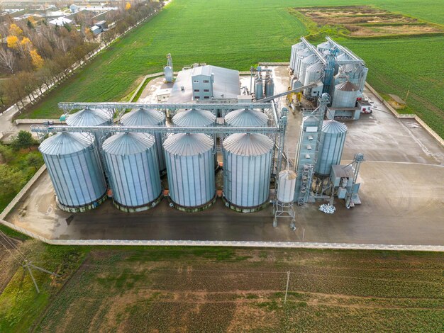 Silver silos on agro manufacturing plant for processing drying cleaning and storage of agricultural products flour cereals and grain Flying a drone over iron barrels of grain quadcopter photo