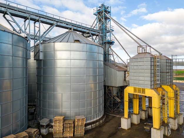 Silver silos on agro manufacturing plant for processing drying cleaning and storage of agricultural products flour cereals and grain Flying a drone over iron barrels of grain quadcopter photo