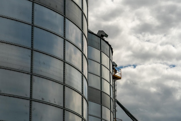 Silver silos on agro manufacturing plant for processing drying\
cleaning and storage of agricultural products flour cereals and\
grain large iron barrels of grain granary elevator