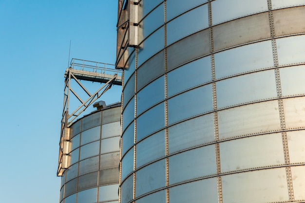 Silver silos on agro manufacturing plant for processing drying cleaning and storage of agricultural products flour cereals and grain Large iron barrels of grain Granary elevator