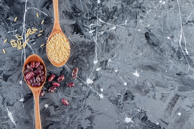 Silver spoons full of long rice and beans on marble background. 