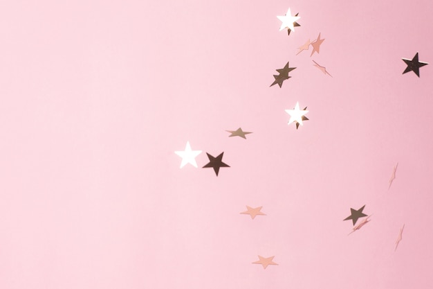 Coriandoli stella d'argento su sfondo rosa pastello.