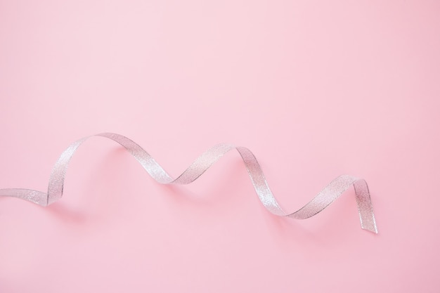 Silver streamers serpentine on pastel pink background. Christmas gift. 