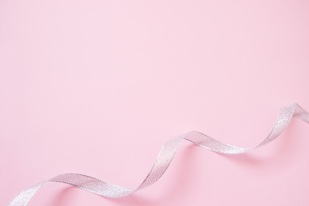 Silver streamers serpentine on pastel pink background. Christmas gift. 