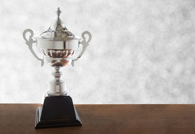 Silver trophy on wooden table isolated over bokeh background. Winning awards with copy spa