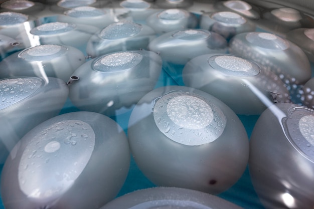 Фото Серебряные воздушные шары, наполненные водой, частично погруженные в воду и с каплями на поверхности