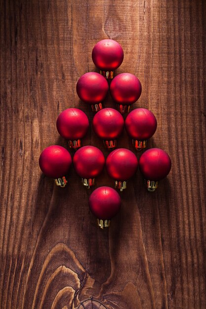 Символ елки из композиции красных новогодних шаров на старой деревянной доске