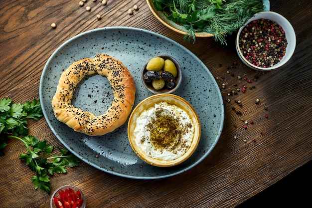 Simit with feta cheese mousse with olive oil and spices, served on blue plate with olives. Wood background. Bagel