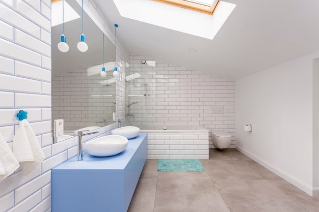 Simple bathroom in the attic with blue washbasin cabinet toilet and bathtub against white brick wall