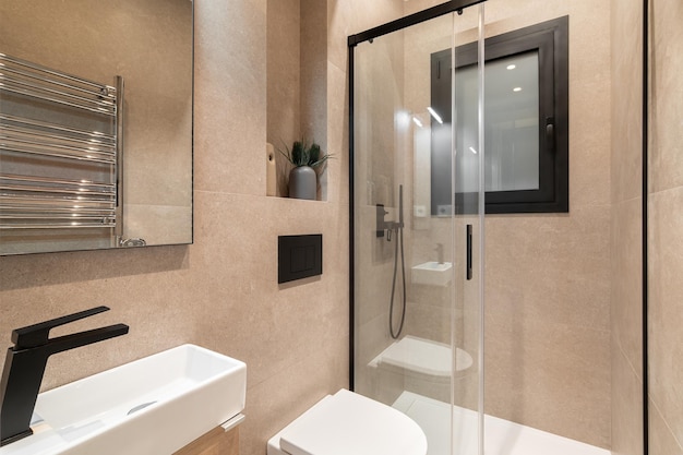 Simple bathroom with black faucet white toilet wooden furniture and beige tiles.