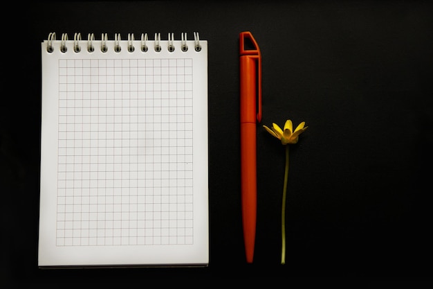 Фото Простой пустой белый блокнот с ручкой и цветком на черном фоне, место для текста