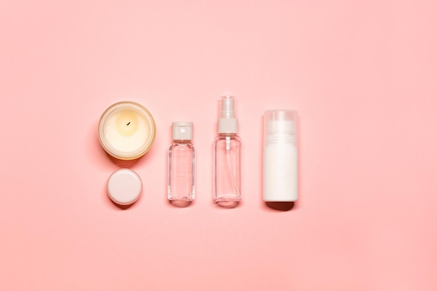 simple composition face lotion toner cream lip balm and a lighted candle on a pink background