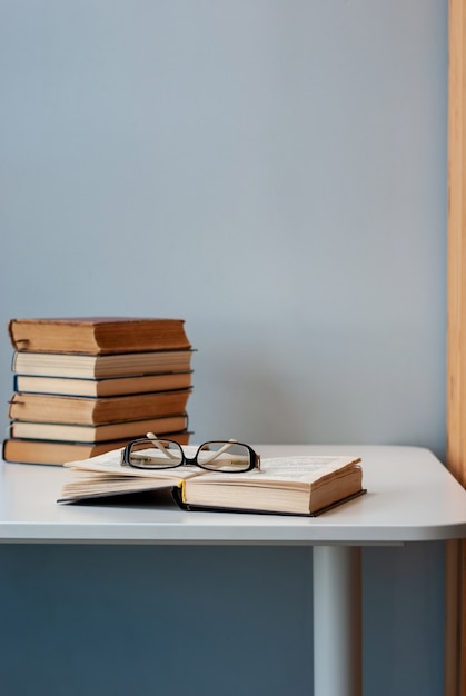 A simple composition of several old books on a white modern table with light gray background, back to school, education. One book is opened with glasses on top