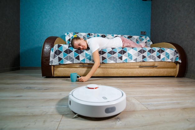 Simple and easy cleaning with modern technology for the household. Girl drinks tea and rests while the vacuum cleaner does the cleaning of the house