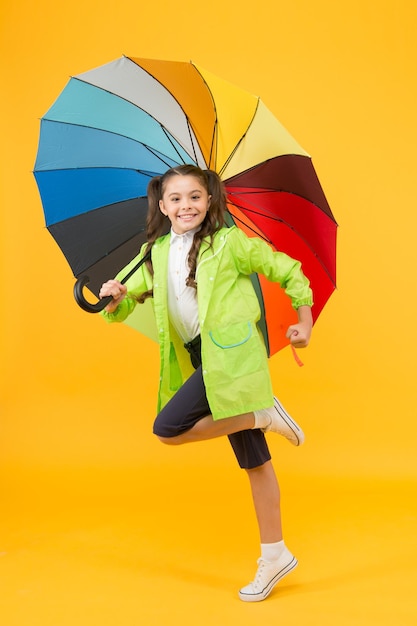 シンプルな幸せ。私は気にしない。屈託のない女子高生が傘防水レイン コートでジャンプします。秋の雨。雨の日の明るいアクセサリー。防水服を着ていれば、雨はそれほど悪くありません。