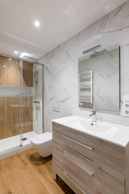 シンプルでモダンなバスルーム、大理石の白いタイル、木製仕上げのトイレとシャワー