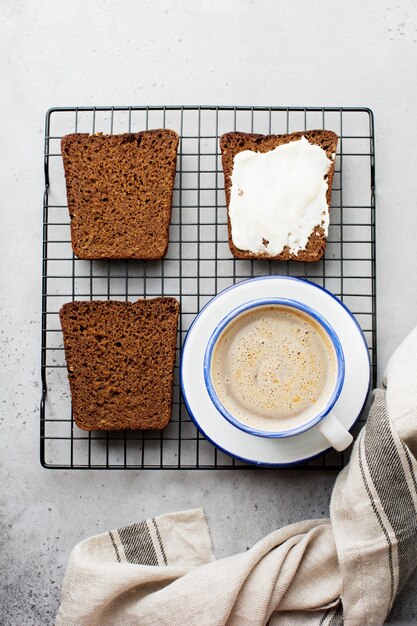 Simple sandwich with cream cheese and cup of coffee for breakfast on stand on old gray surface