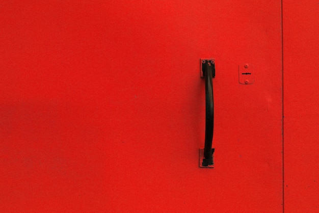 Фото Простая стальная дверь, окрашенная в красную краску с черной пластиковой ручкой.