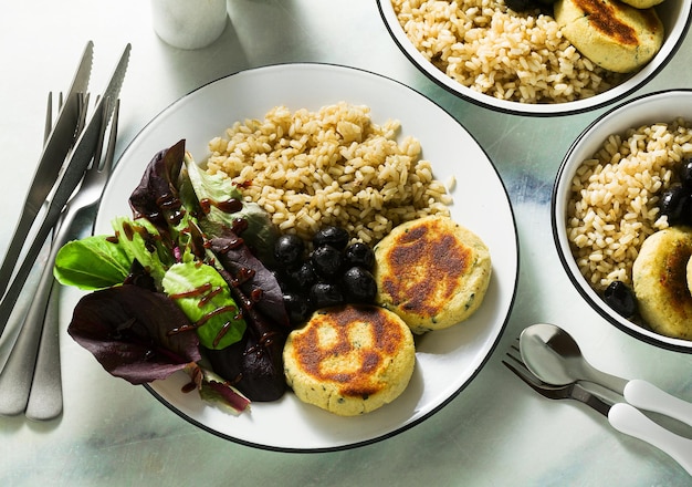 Un semplice pranzo o una cena vegana per una famiglia di due adulti e un bambino di riso integrale con okara di soia e polpette di patate con insalata fresca e olive su un tavolo di marmo