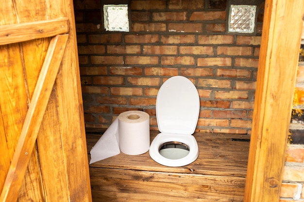 Una semplice toilette da villaggio con un enorme rotolo di carta igienica e un grande rotolo di carta igienica nella toilette.