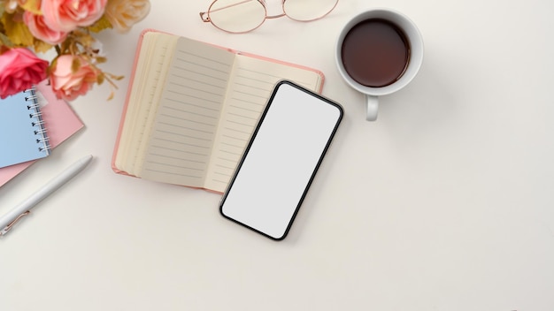 Photo a simple white workspace with notebook coffee cup and smartphone blank screen mockup top view