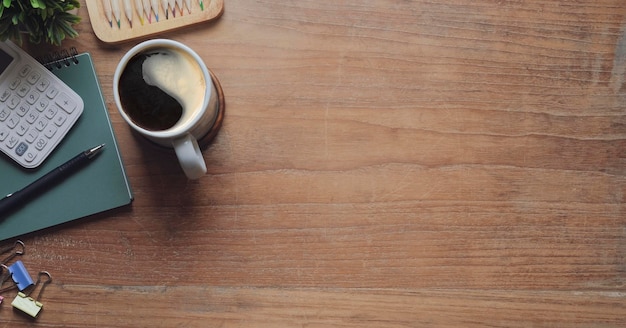 Posto di lavoro semplice con calcolatrice per tazza di caffè e taccuino su scrivania in legno vista dall'alto con spazio per la copia