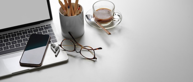 Simple workspace with copy space, mock up laptop, coffee cup, stationery, smartphone and eye glasses