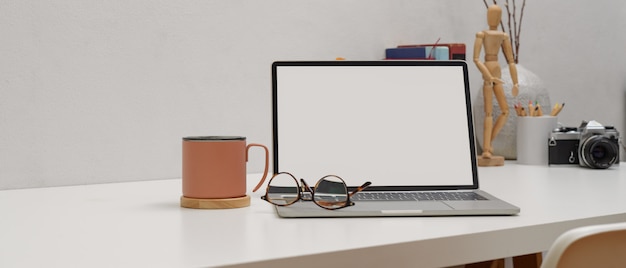 Simple worktable with mock up laptop, glasses, mug and supplies on white table with white chair