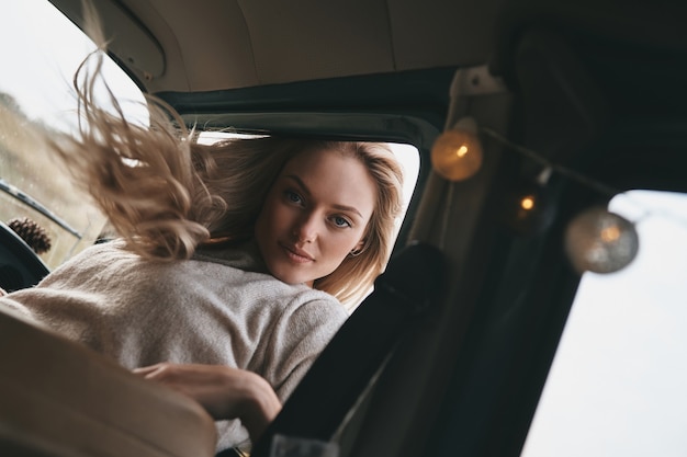 Simply carefree. Attractive young smiling woman leaning out the van?s window and looking at camera while enjoying the car travel