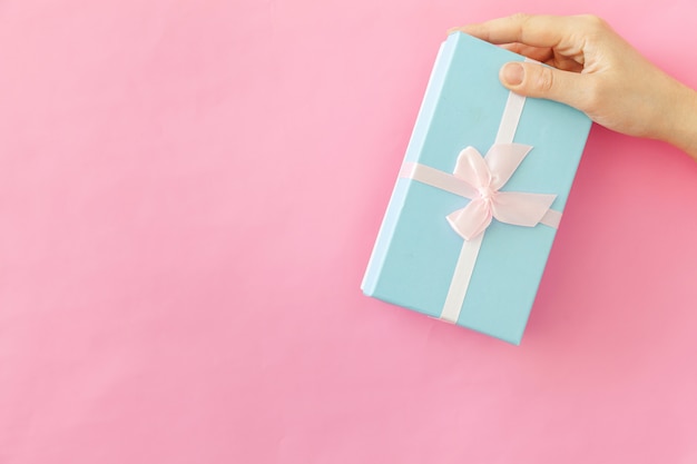 Simply design female woman hand holding blue gift box isolated on pink pastel colorful trendy background