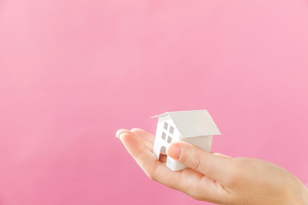 Simply design female woman hand holding miniature white toy house isolated on pink pastel colorful trendy background. Mortgage property insurance dream home concept. Copy space