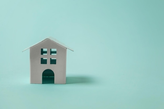 Простой дизайн с миниатюрным белым игрушечным домиком, изолированным на синем пастельно-красочном модном фоне. Ипотечное страхование имущества. Концепция дома мечты.