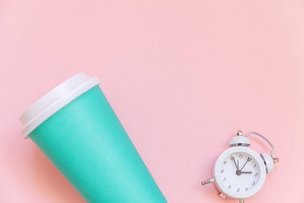 ピンクの背景に分離された単純なフラットレイ青い紙のコーヒーカップと目覚まし時計