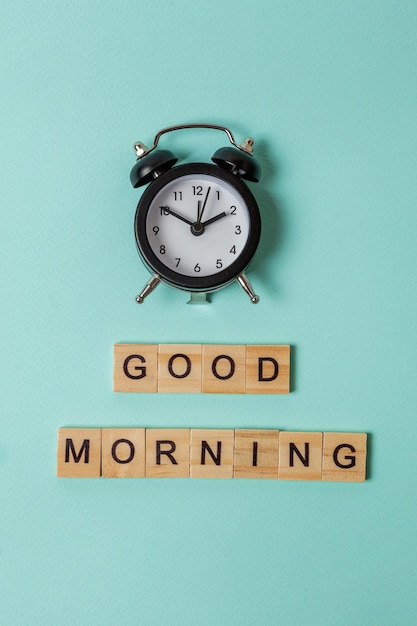 Simply flat lay design alarm clock and Inscription GOOD MORNING letters word on blue pastel colorful trendy background Breakfast time Good morning wake up awake concept Top view copy space