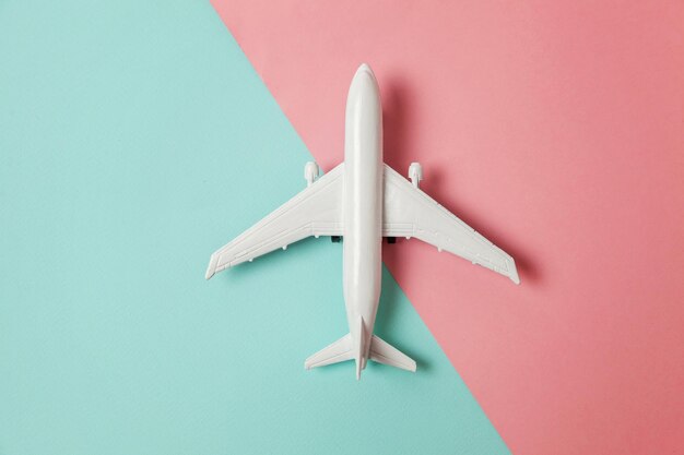 Simply flat lay design miniature toy model plane on blue and\
pink pastel colorful paper trendy geometric background travel by\
plane vacation summer weekend sea adventure trip concept