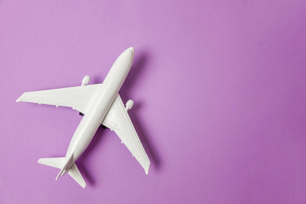 Simply flat lay design miniature toy model plane on violet purple pastel colorful paper trendy background Travel by plane vacation summer weekend sea adventure trip journey ticket tour concept