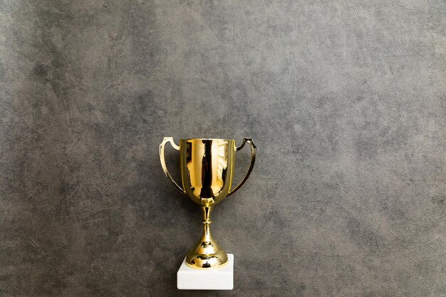 Simply flat lay design winner or champion gold trophy cup on concrete stone grey background victory
