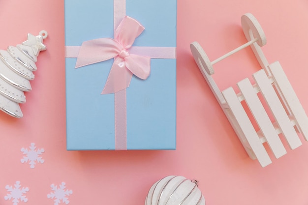 ピンクのパステルカラーのトレンディな背景に分離されたシンプルな最小限の構成の冬のオブジェクト飾りボールモミの木そりギフトボックス。お祝いのコンセプトのためのクリスマス新年12月の時間。フラットレイトップビュー