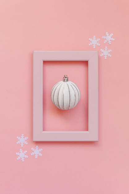 Simply minimal composition winter objects ornament ball in pink frame isolated on pink pastel trendy background. Christmas New Year december time for celebration concept. Flat lay top view