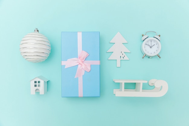 Simply minimal composition winter objects ornament sled fir tree ball gift box isolated blue pastel background. 
