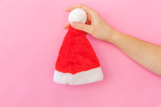 Simply minimal design female woman hand holding Christmas ornament Santa hat isolated on pink pastel colorful trendy background