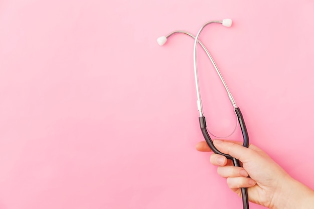 트렌디한 파스텔 핑크색 배경에 격리된 의학 장비 청진기나 폰도스코프를 들고 있는 최소한의 디자인 여성입니다. 의사를 위한 기구 장치. 건강 관리 생명 보험 개념