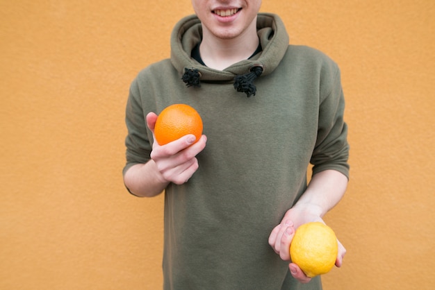 Sinaasappel en citroen in de handen van een jonge man die op een oranje muur. Concept Fruit