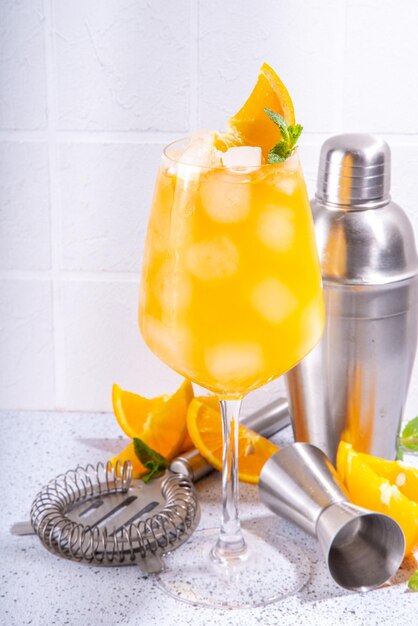 Sinaasappel en munt alcohol cocktail aperol spritz mimosa drankje in lang cocktailglas met verse sinaasappelschijfje garneer wit betegelde achtergrond met bar gebruiksvoorwerpen kopie ruimte